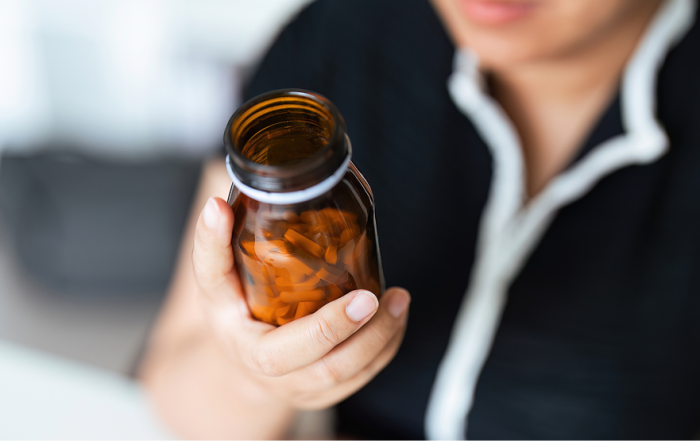 Person holding up an amber bottle full of vitamins.