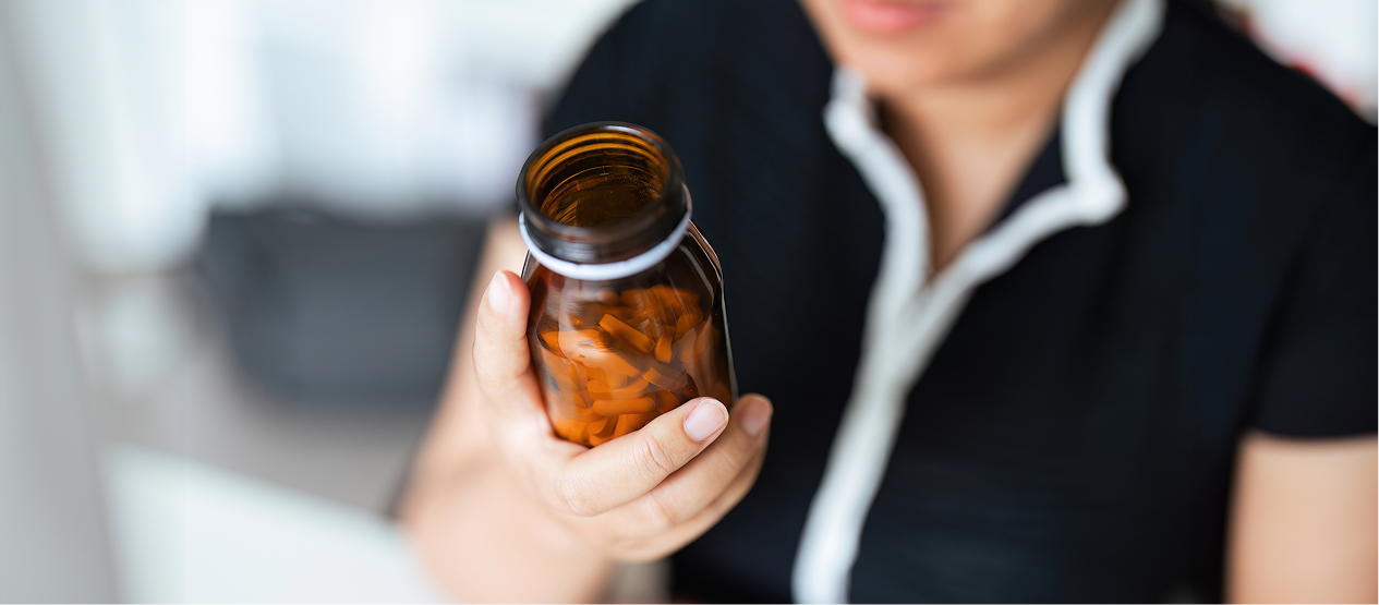 Person holding up an amber bottle full of vitamins.